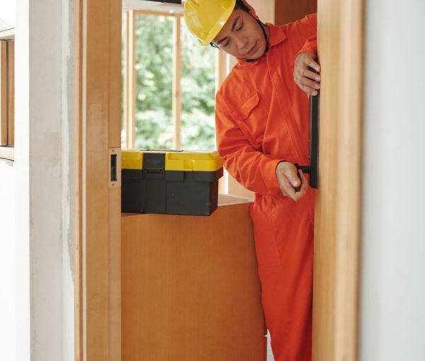 Workman in orange overall fixing smart electronic door lock